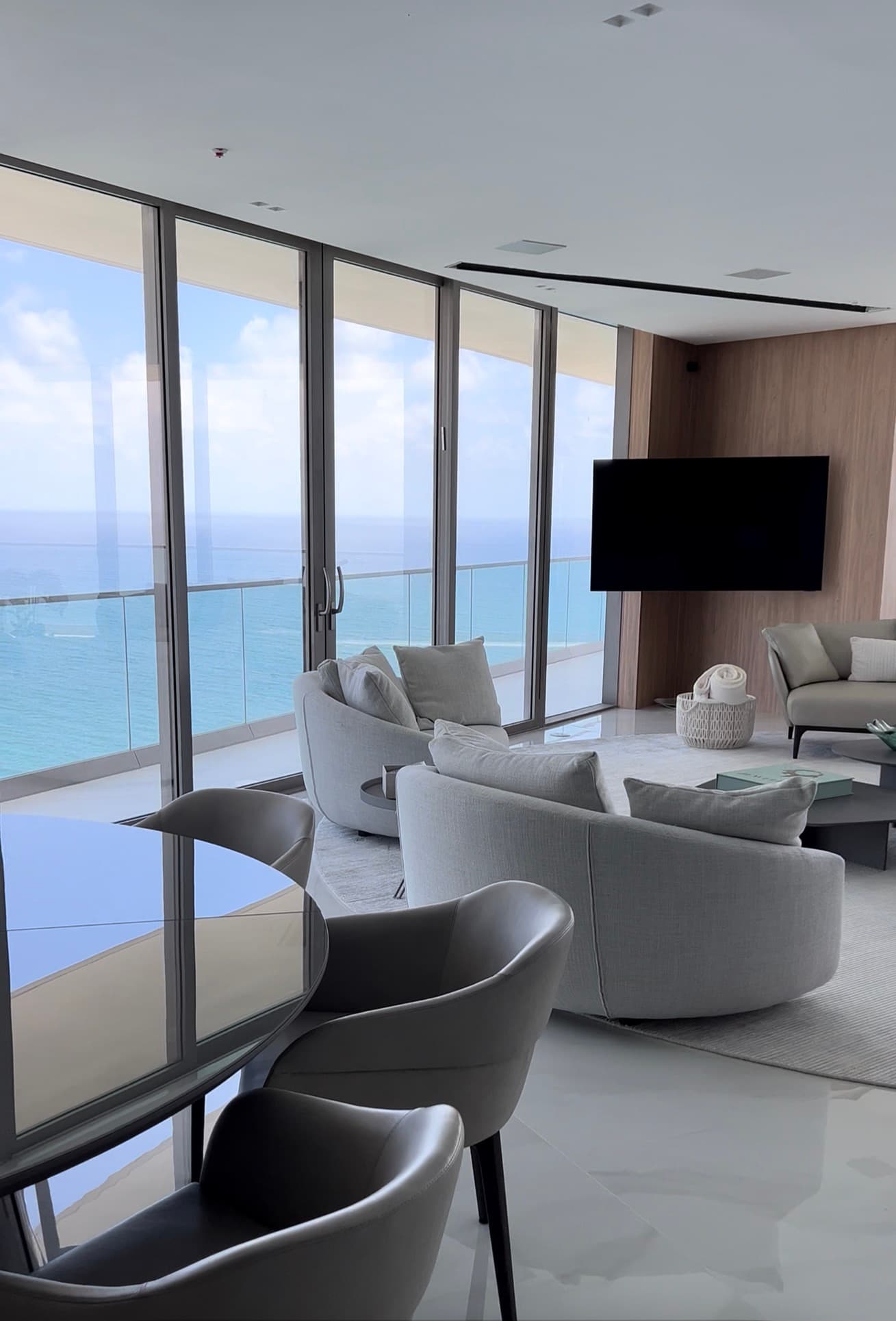 An oceanfront living room with a full-height wood-panelled media wall and concealed ceiling detail.