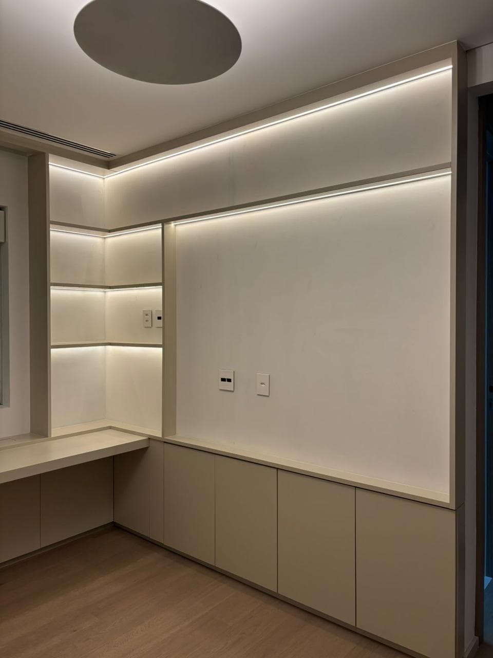 A low blackened-oak credenza against a fluted white wall panel, beside a linen headboard on a herringbone floor.
