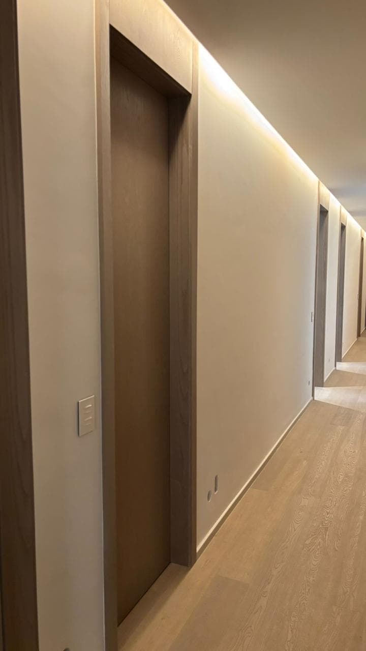 A corridor lined with flush oak-framed doorways under a continuous cove light.