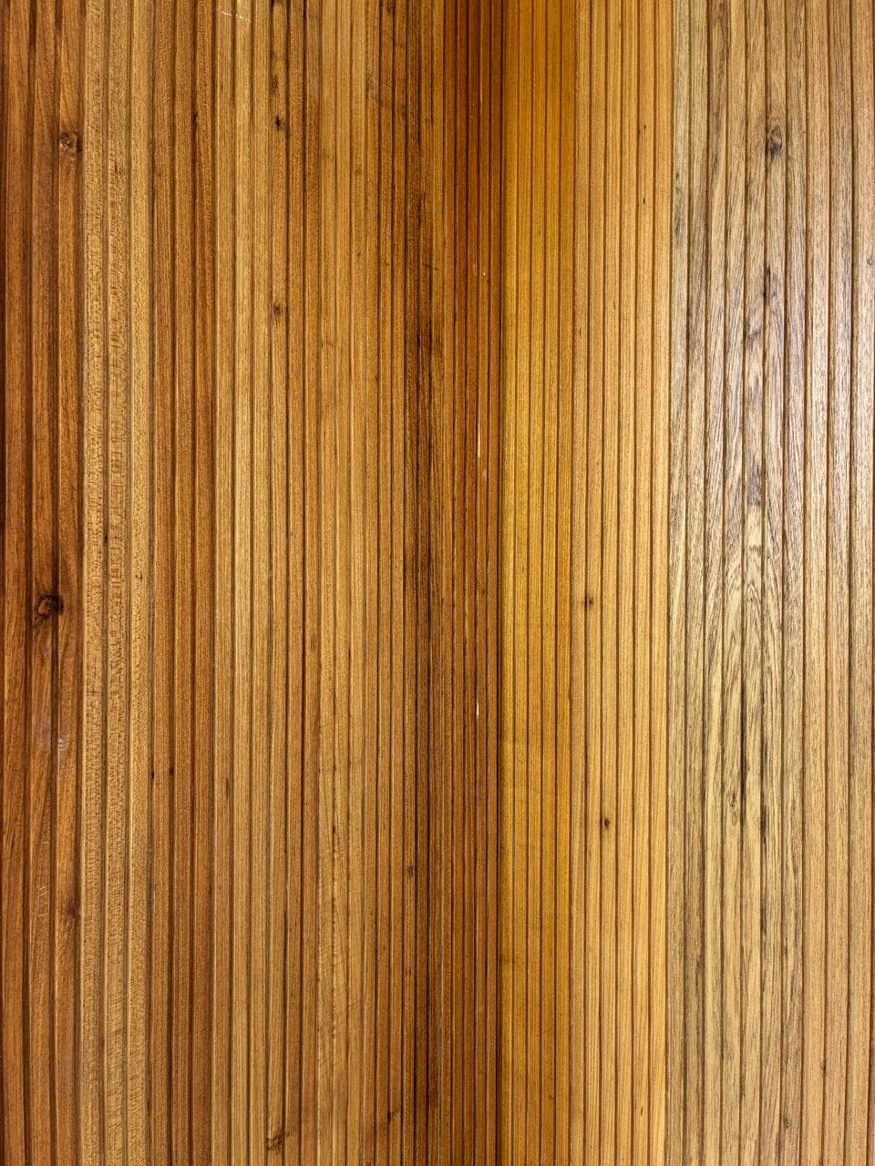 A close view of a solid teak slatted panel, grain and tone varying across the run.