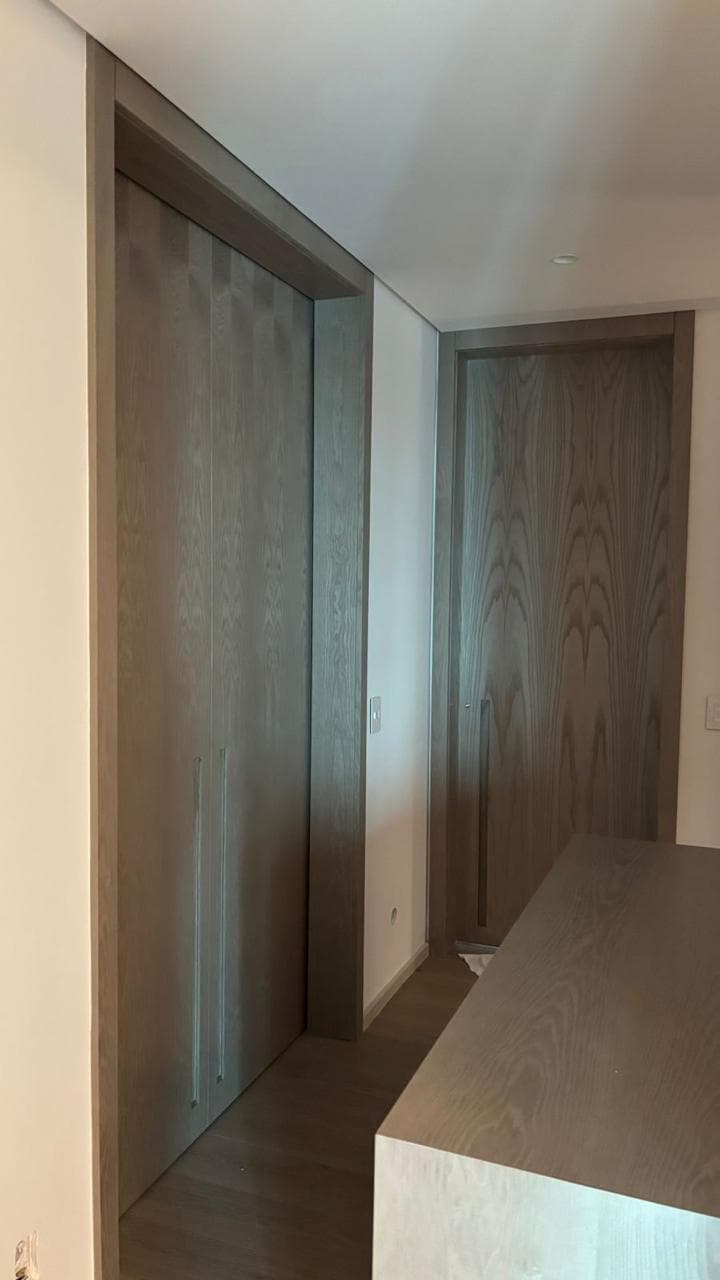 Tall oak wardrobe doors with book-matched grain and full-height recessed pulls, beside a matching passage door.